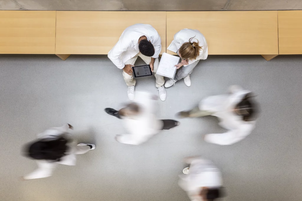 Szene in einem Krankenhaus, fotografiert von oben. Zwei Personen Meeting und weitere Personen laufen vorbei